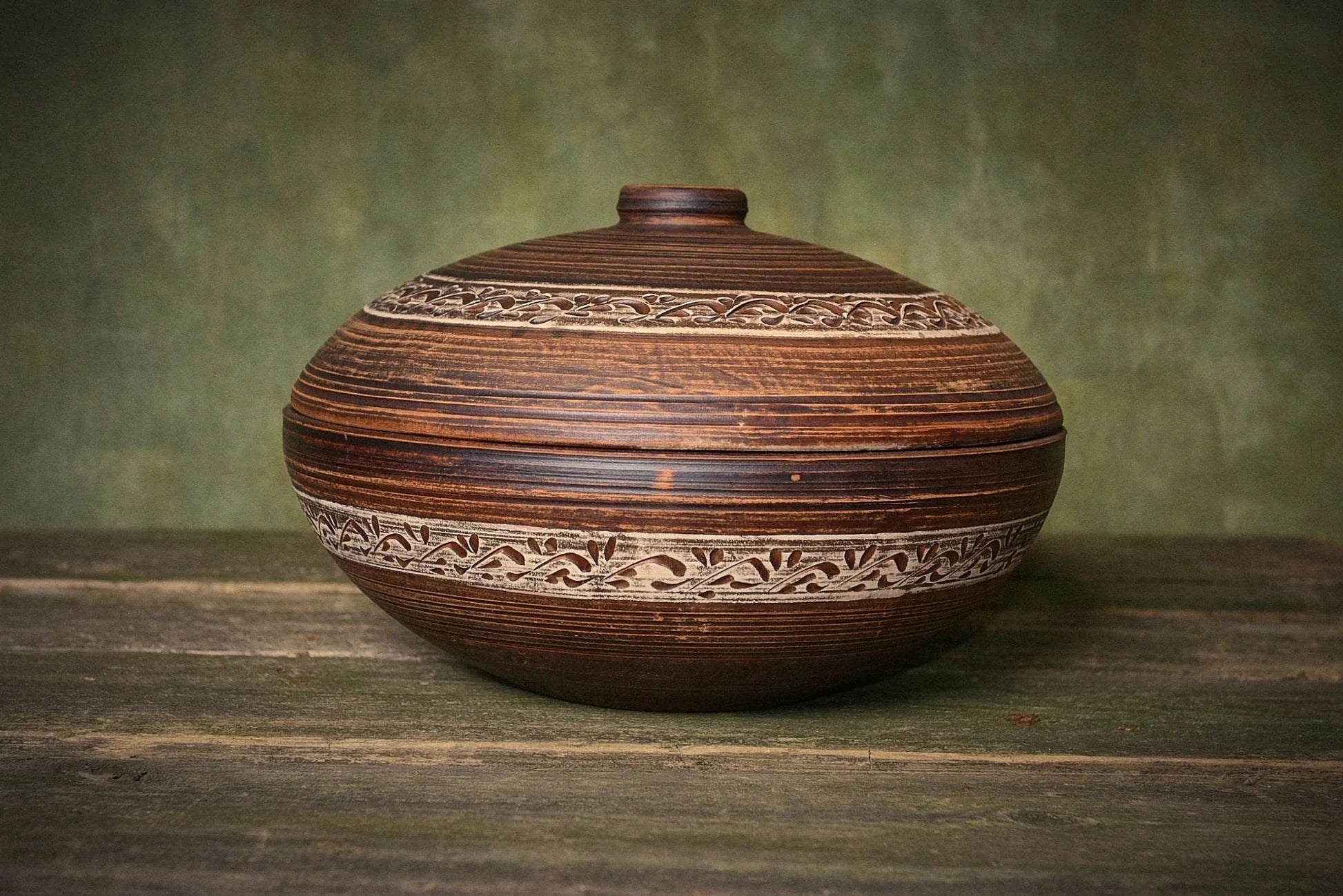 Handmade ceramic clay pot with lid and decorative carvings on rustic wood table