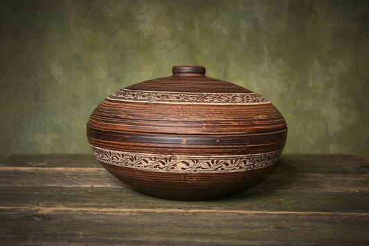 Handmade ceramic clay cooking pot with lid and carved pattern on rustic wooden table