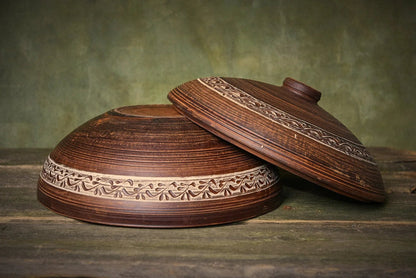 Handmade ceramic baking dish with lid, rustic clay pot featuring carved patterns on wood surface