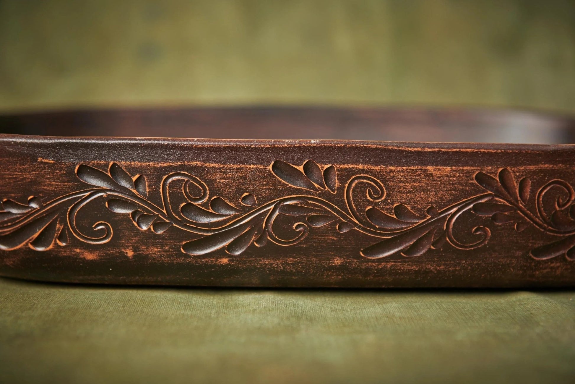 Handmade brown ceramic baking tray with carved floral pattern on green background