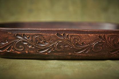 Handmade brown ceramic baking tray with carved floral pattern on green background