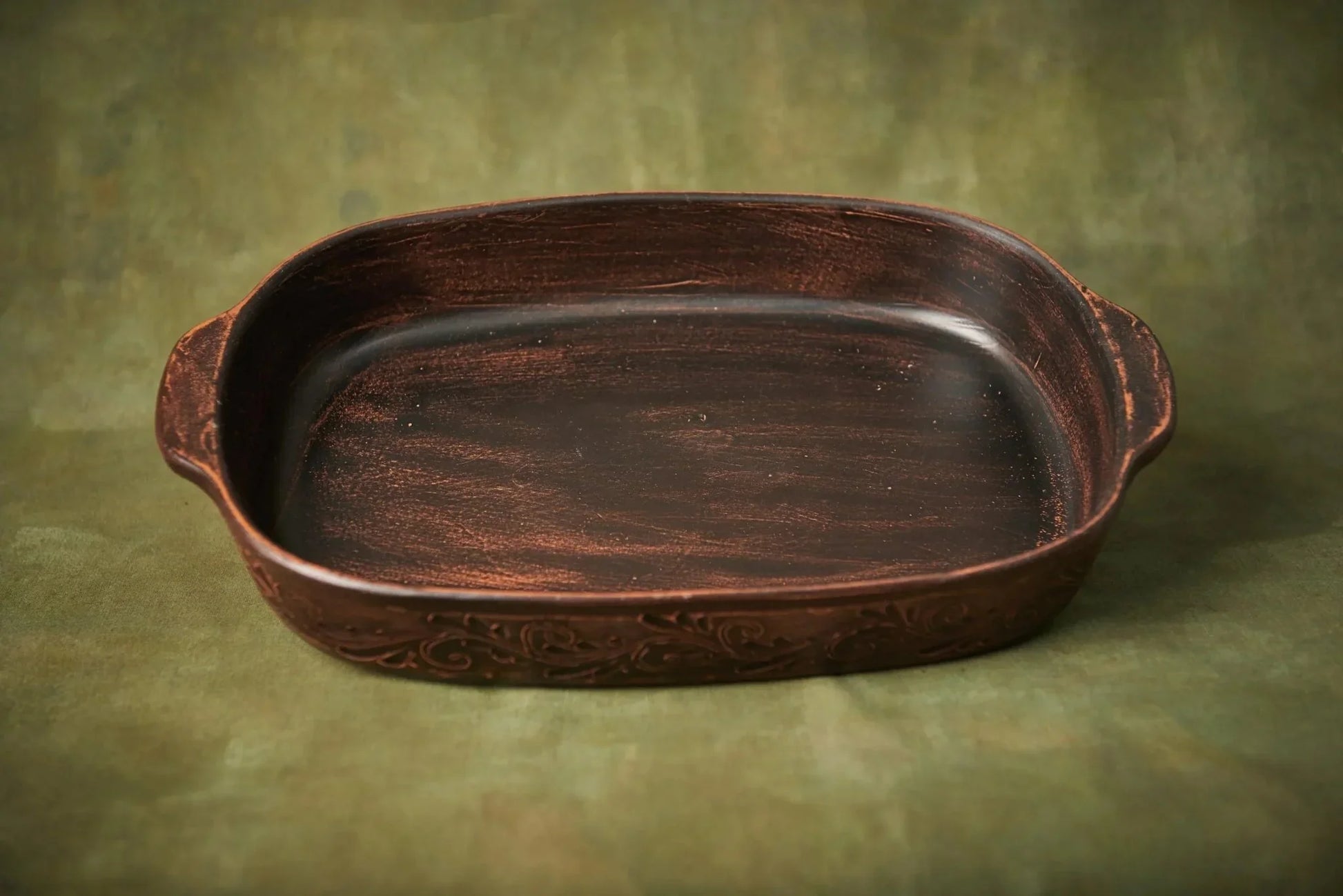 Handmade brown ceramic baking tray with artistic pattern, artisan pottery dish on green background