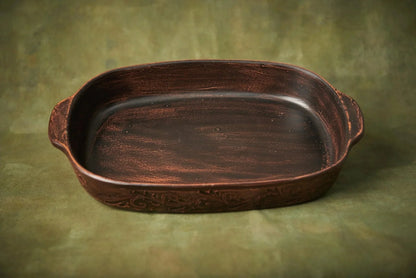 Handmade brown ceramic baking tray with artistic pattern, artisan pottery dish on green background