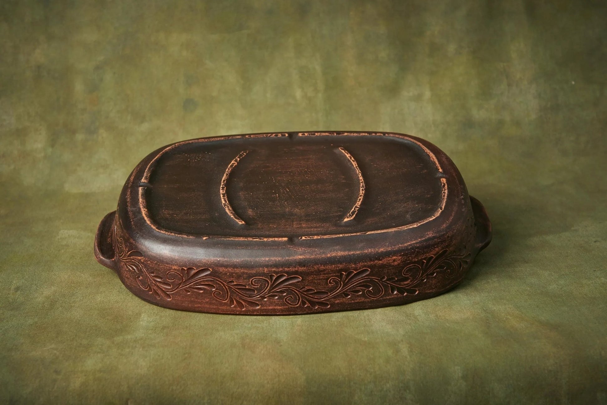 Handmade ceramic baking tray with embossed floral design on a green background