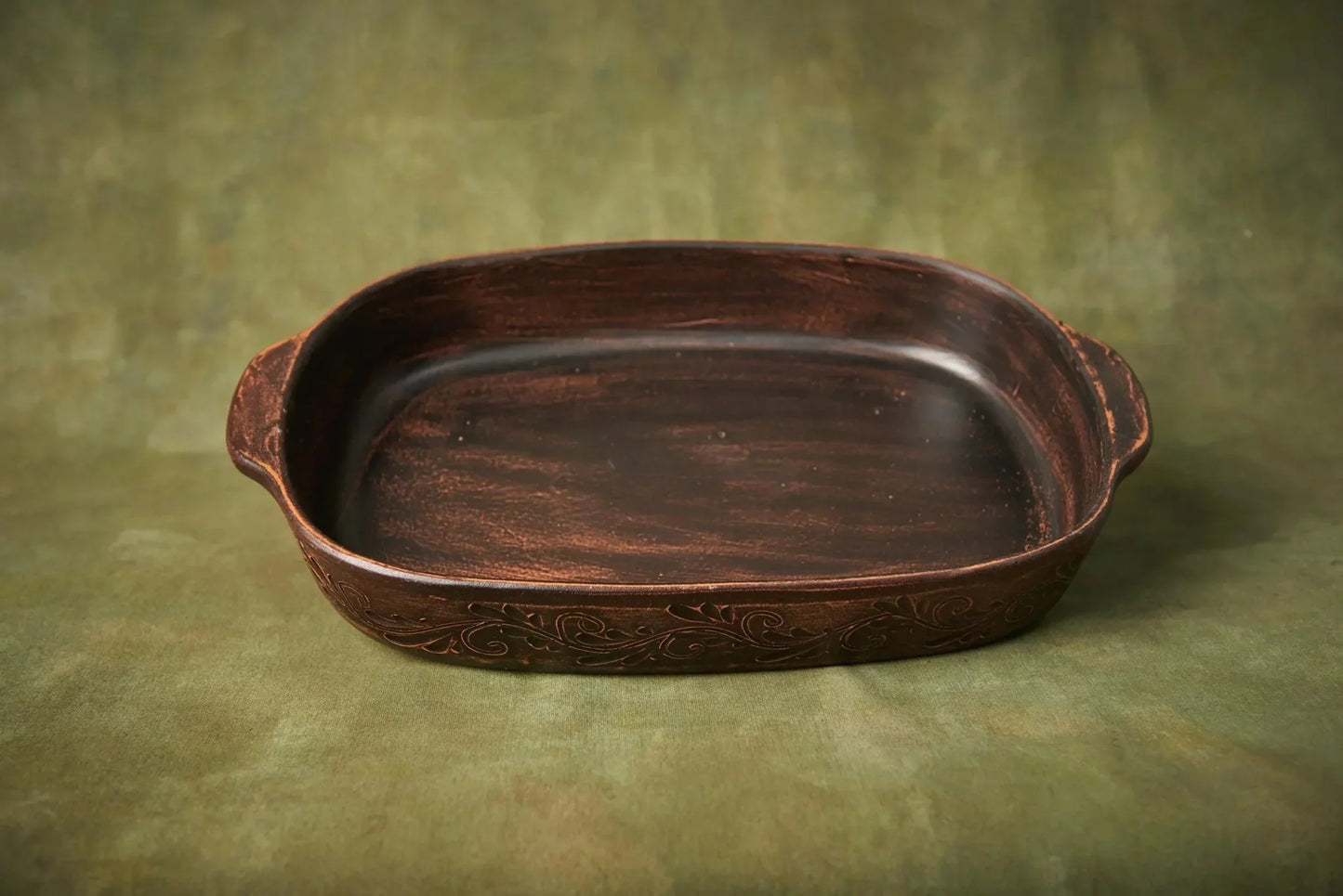 Handmade ceramic baking tray with etched design, artisan pottery serving dish on green backdrop