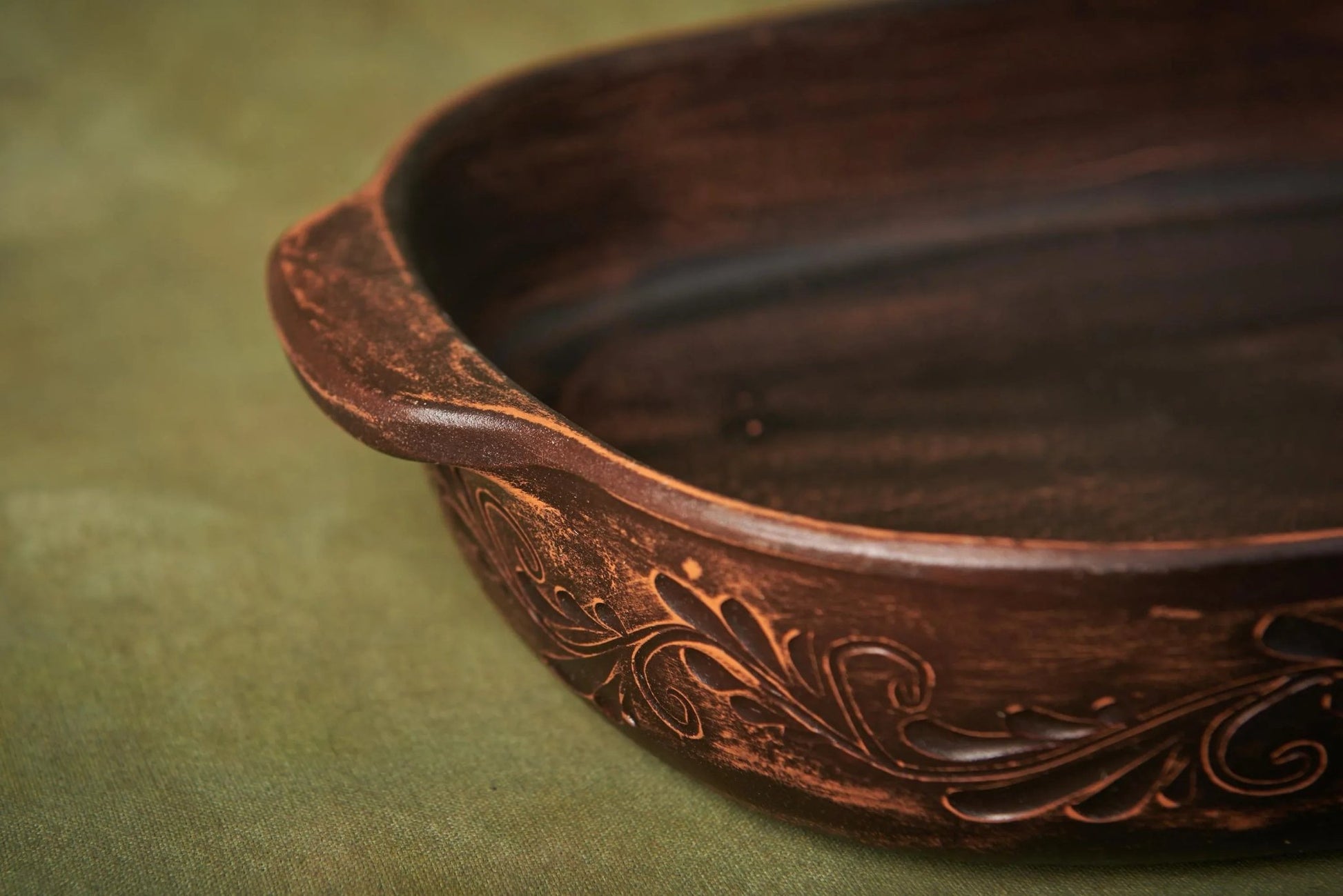 Handmade ceramic baking tray with decorative embossed pattern on a green surface