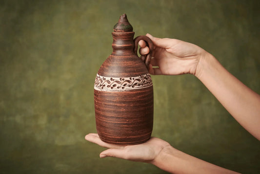 Hand holding a handmade ceramic amphora with handle and lid, rustic clay water or wine jug