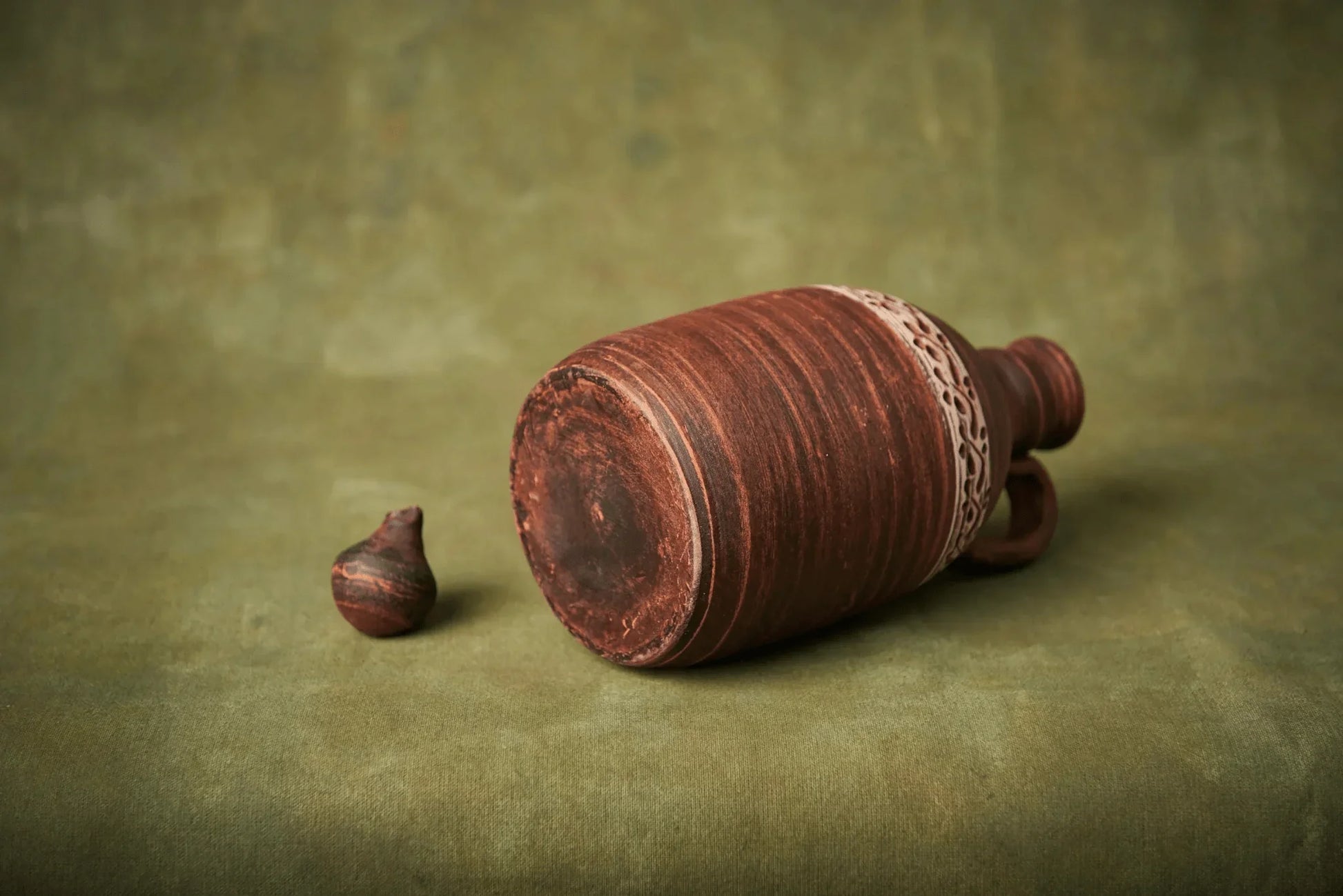 Handmade ceramic amphora with handle and lid on green background, clay pottery vessel
