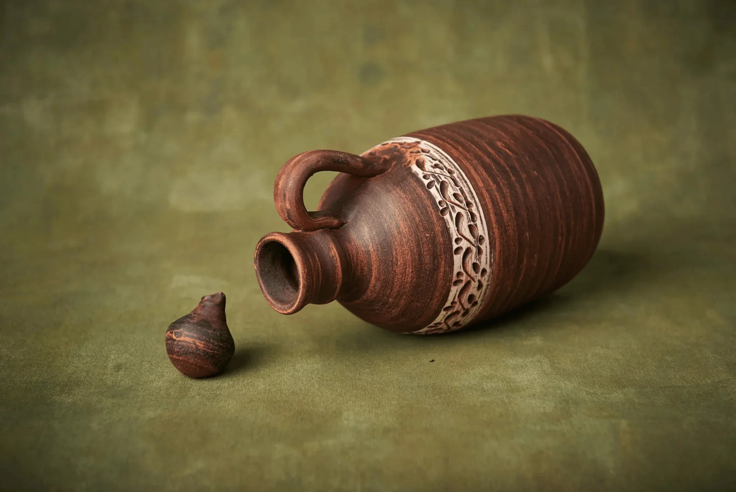 Handmade ceramic bottle with handle and decorative band, clay jug with lid, on green background