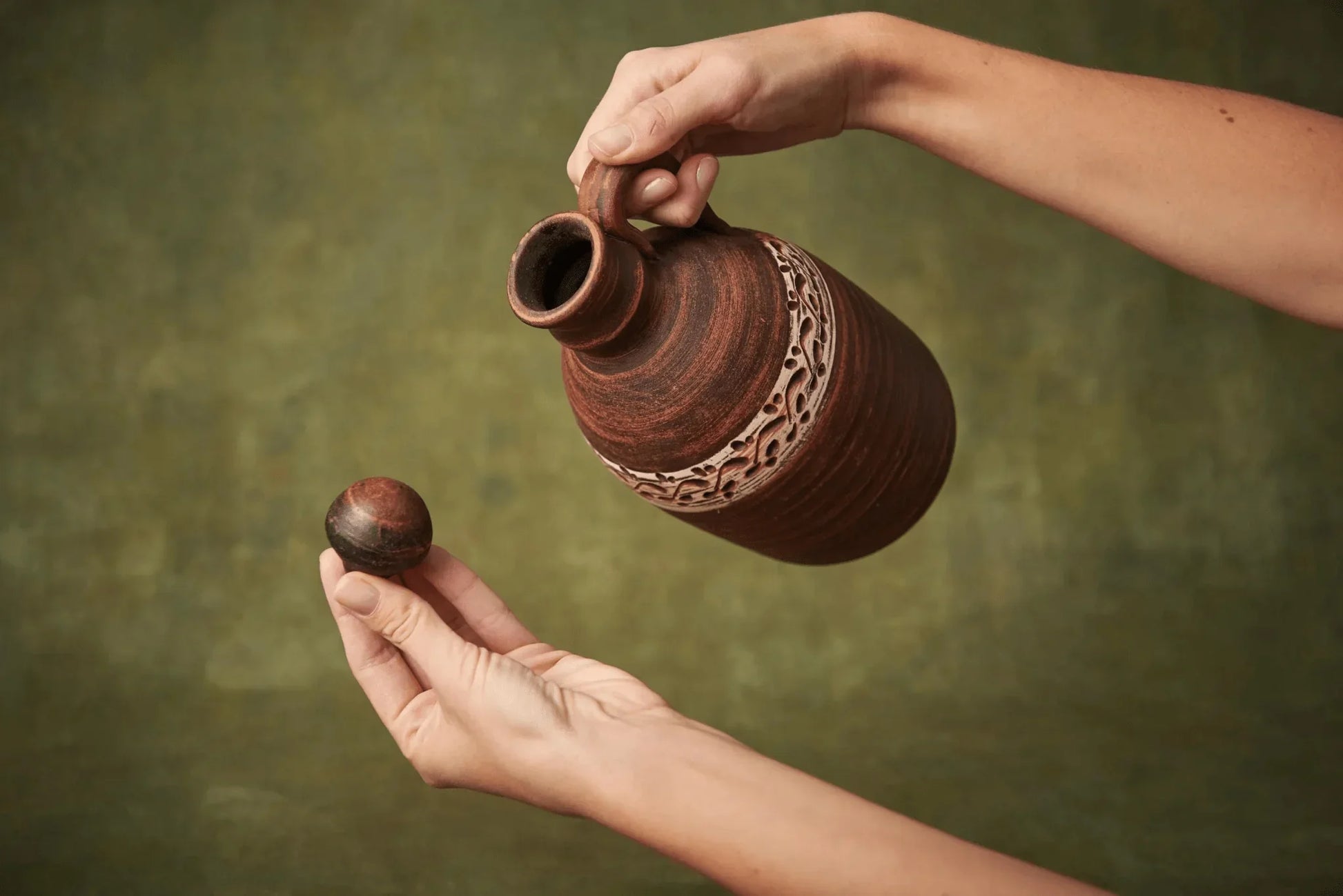 Hand holding handmade ceramic amphora clay bottle with handle and lid, artisan pottery vessel