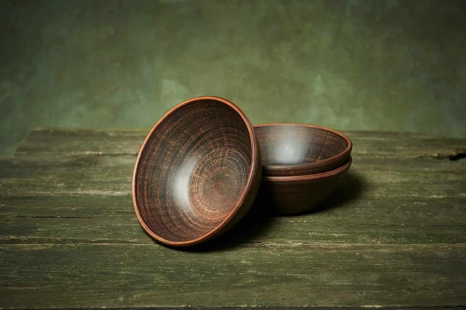 Set of three handmade deep red clay ceramic bowls on rustic wooden surface