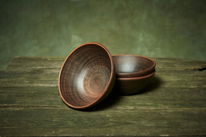 Set of three handmade deep red clay ceramic bowls on rustic wooden surface