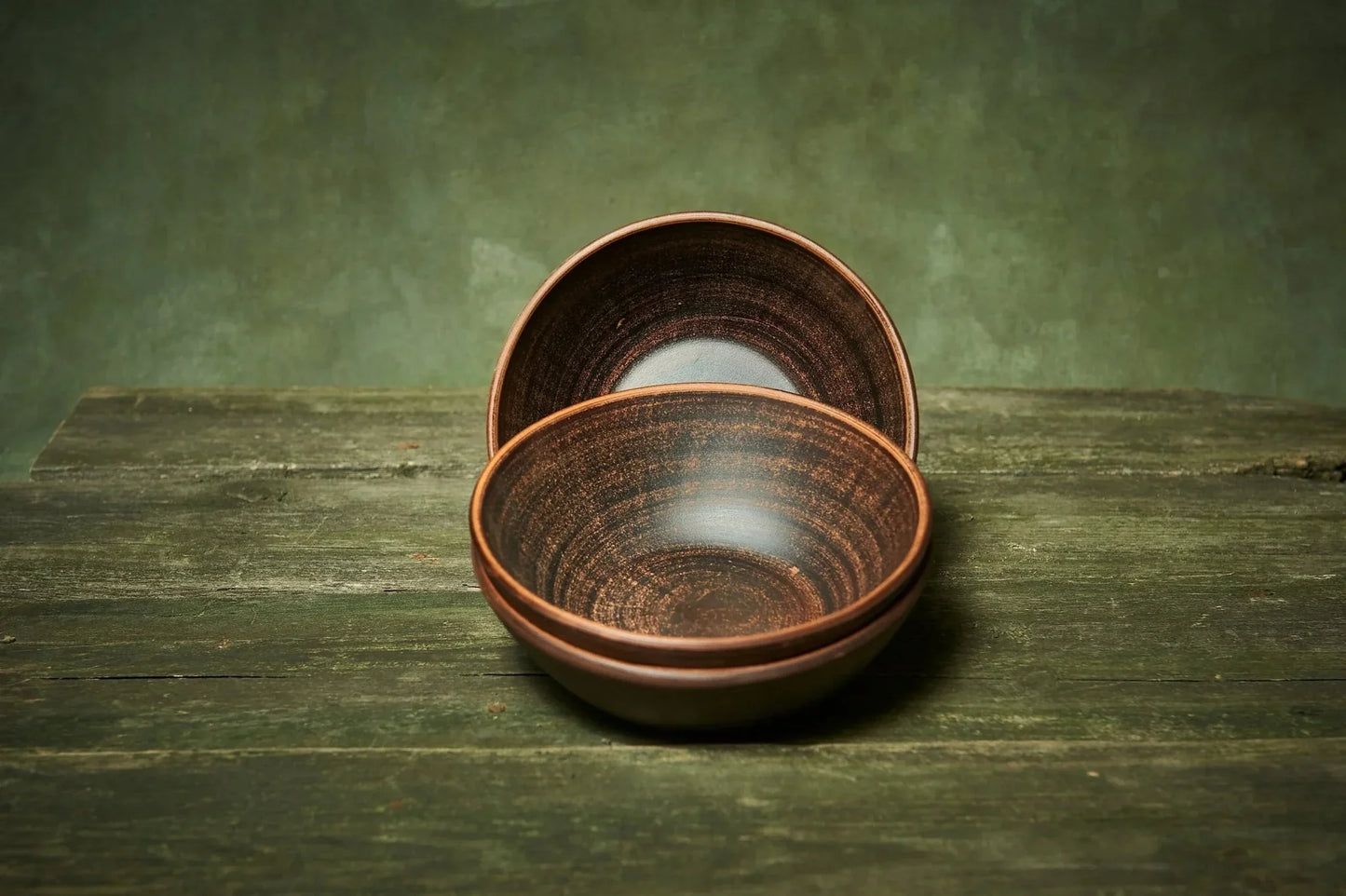 Set of three handmade deep red clay ceramic bowls on rustic wooden surface, Ukrainian pottery