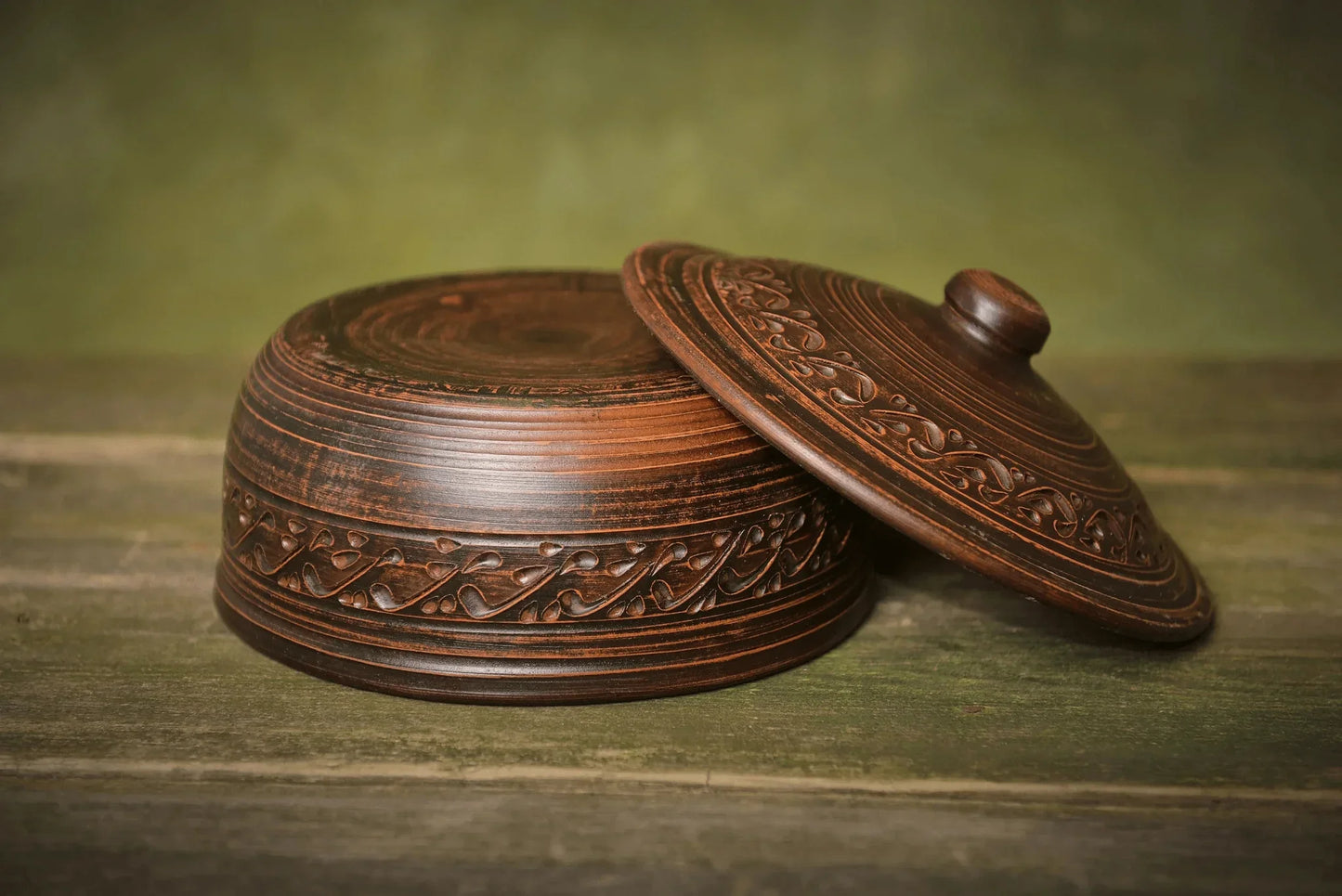 Handmade ceramic bread pot with lid, ornate clay baking dish on rustic wood surface