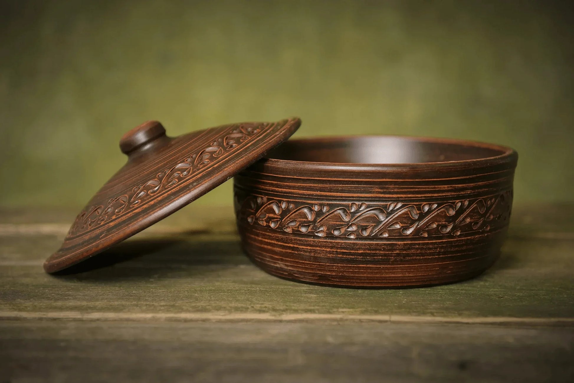Handmade ceramic bread pot with lid and ornate clay detailing on rustic wood surface