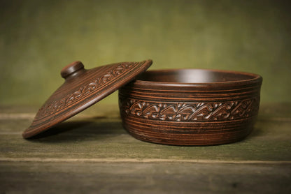 Handmade ceramic bread pot with lid and ornate clay detailing on rustic wood surface