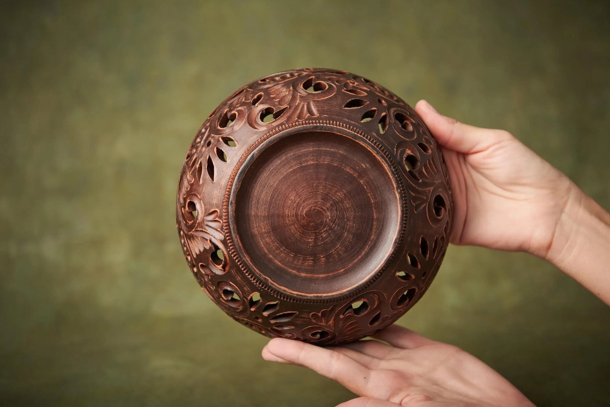 Handmade carved ceramic bowl with cutout designs held in hands, rustic clay home decor