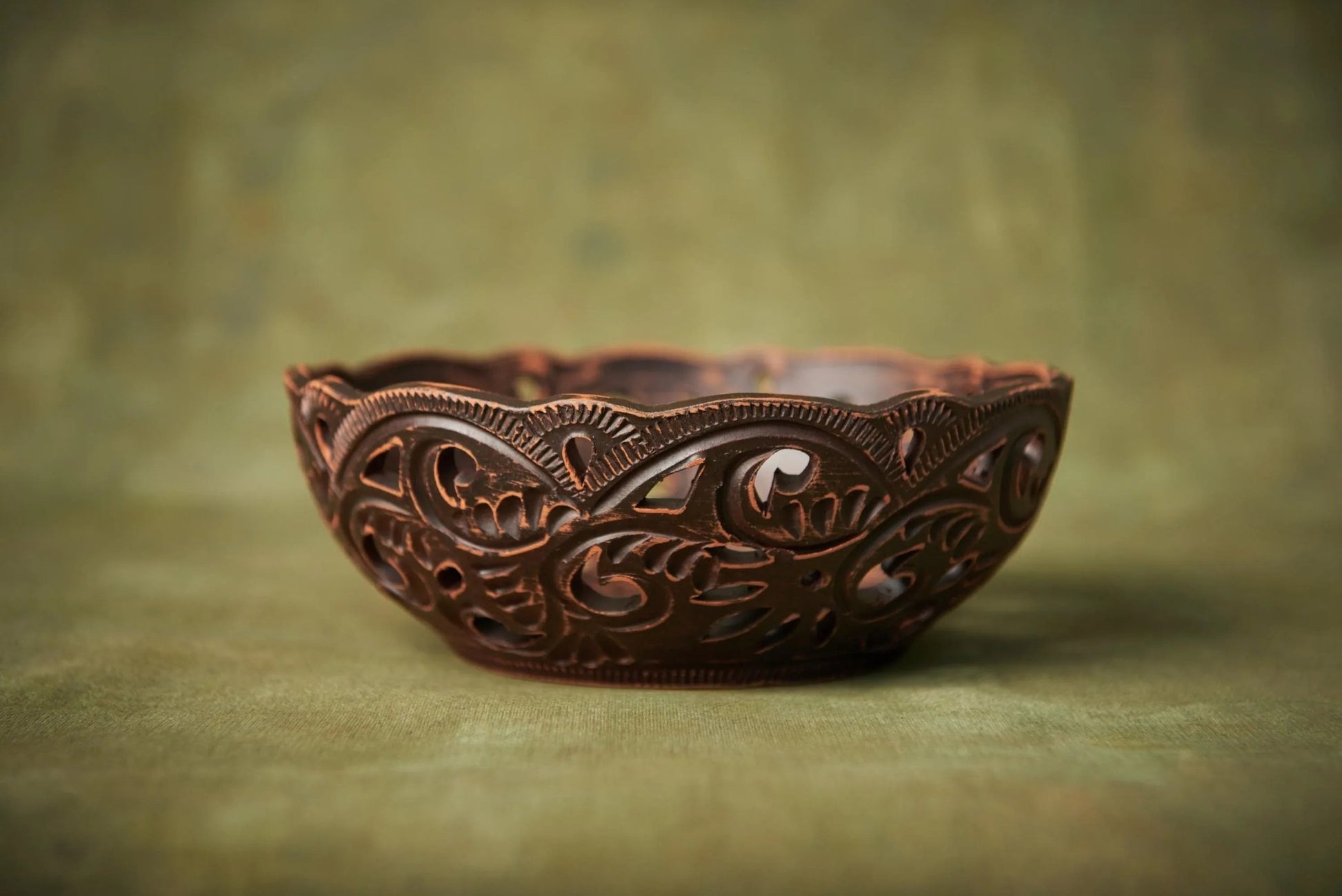 Handmade ceramic carved bowl with intricate patterns, rustic homeware decor on green background