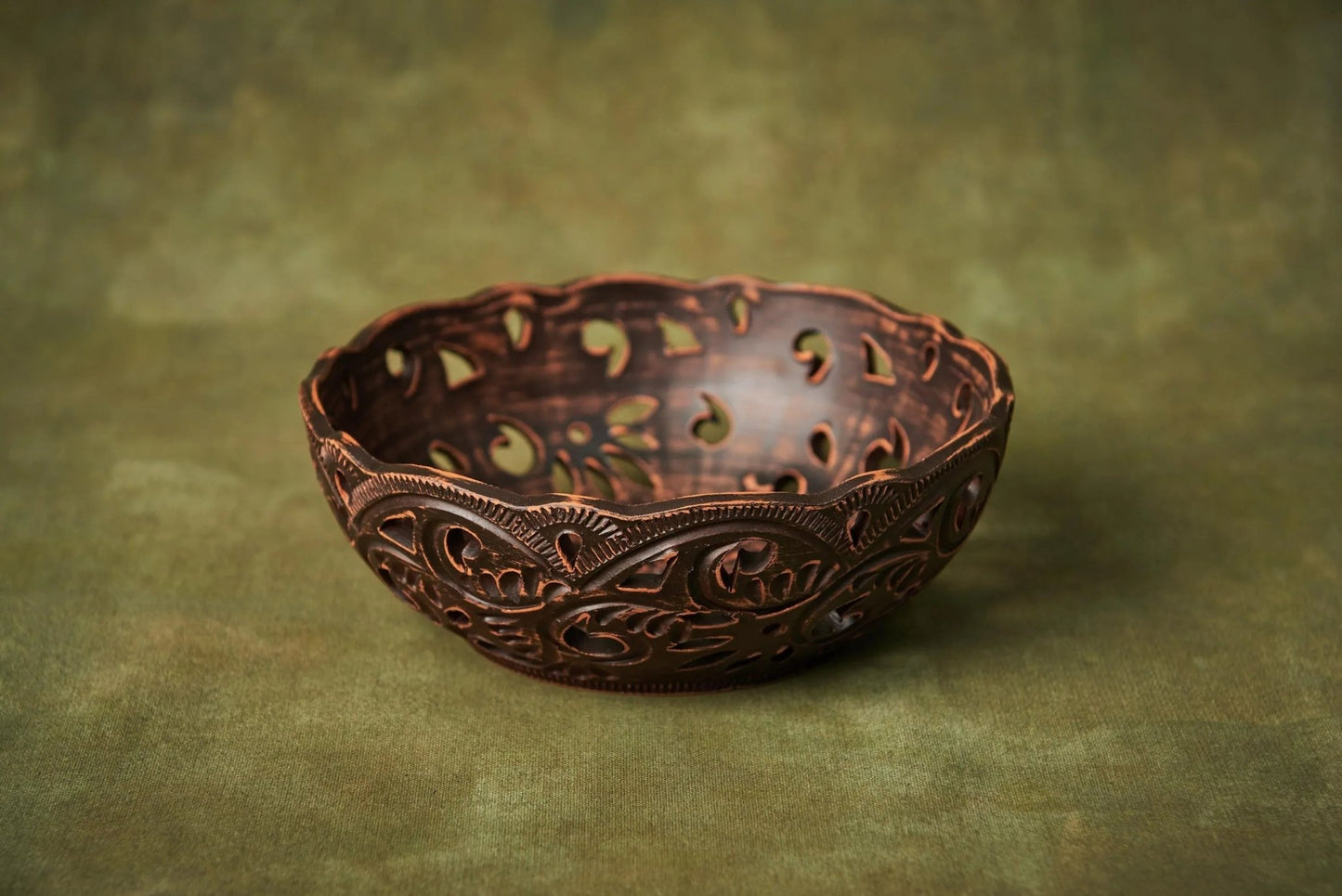 Handmade carved ceramic candy bowl with rustic pattern on a green background
