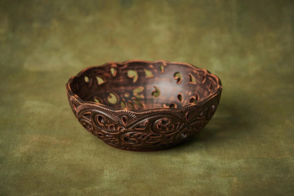 Handmade carved ceramic candy bowl with rustic pattern on a green background