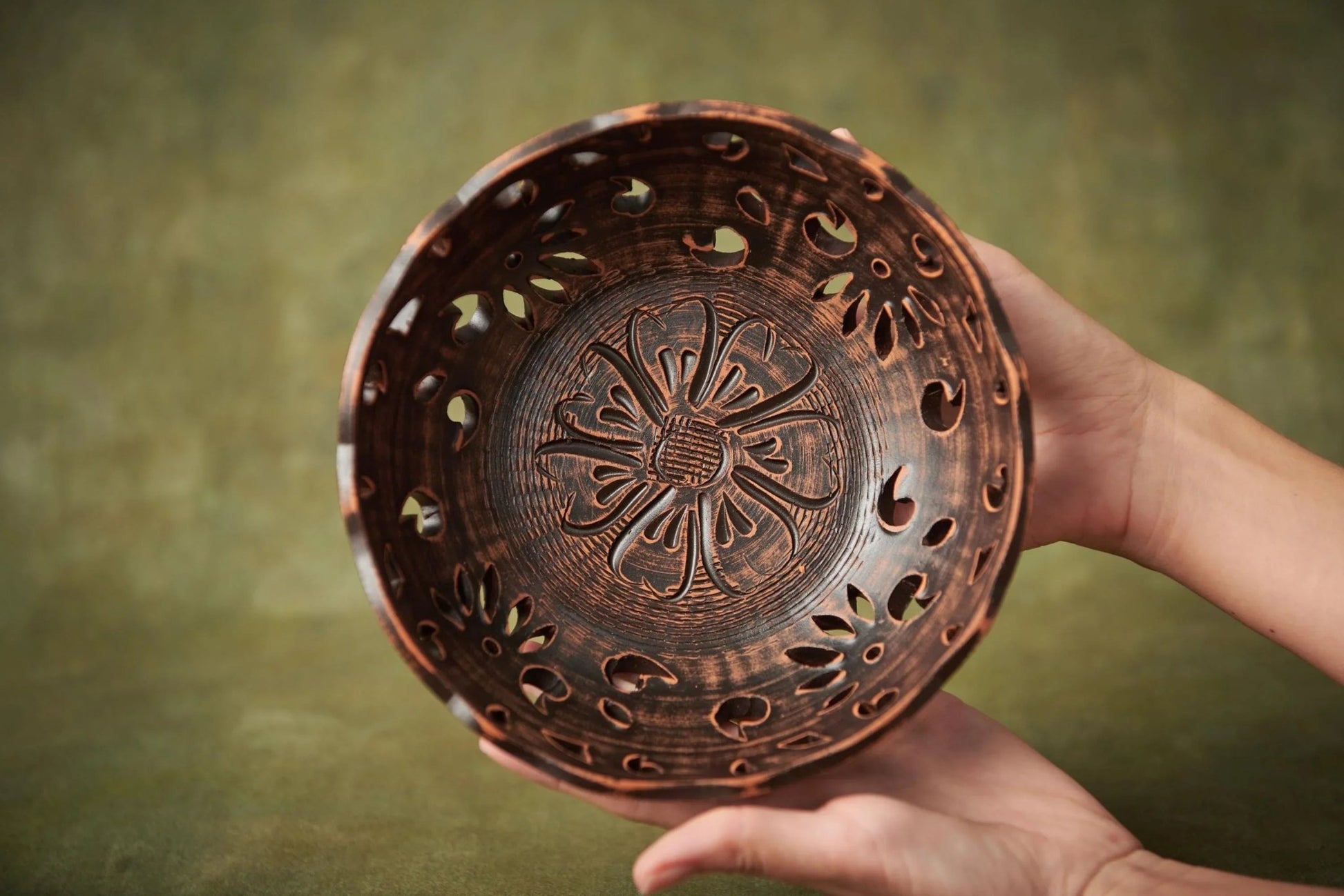 Hand holding a handmade carved ceramic bowl with floral patterns, rustic clay homeware