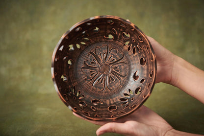 Hand holding a handmade carved ceramic bowl with floral patterns, rustic clay homeware