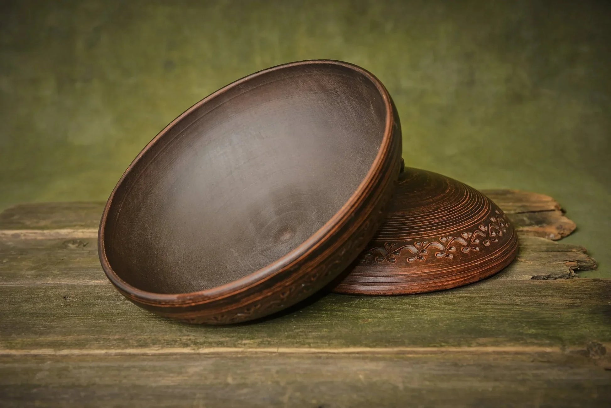 Handmade round clay cooking pot with lid and decorative engraving on rustic wood