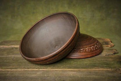Handmade round clay cooking pot with lid and decorative engraving on rustic wood