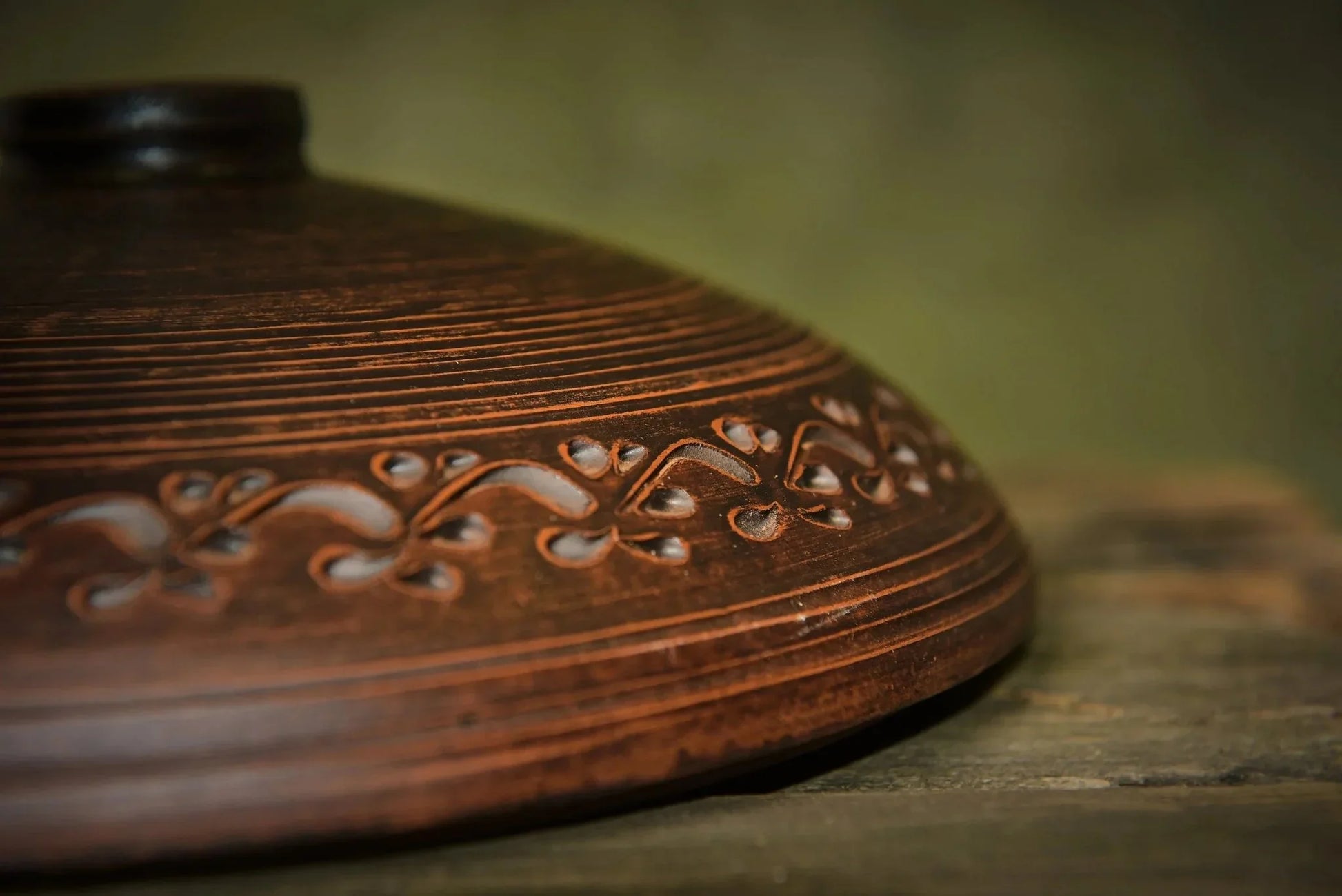 Handmade clay cooking pot lid with decorative carved pattern on rustic wooden surface