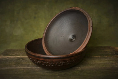 Handmade round clay baking dish with lid, rustic pottery on wooden surface