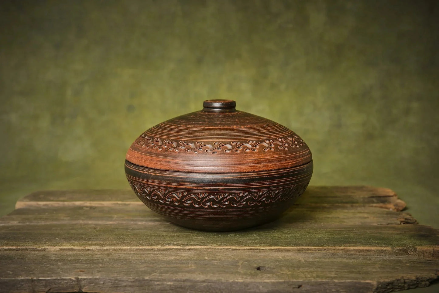 Handmade ceramic clay cooking pot with lid and intricate patterns on rustic wood