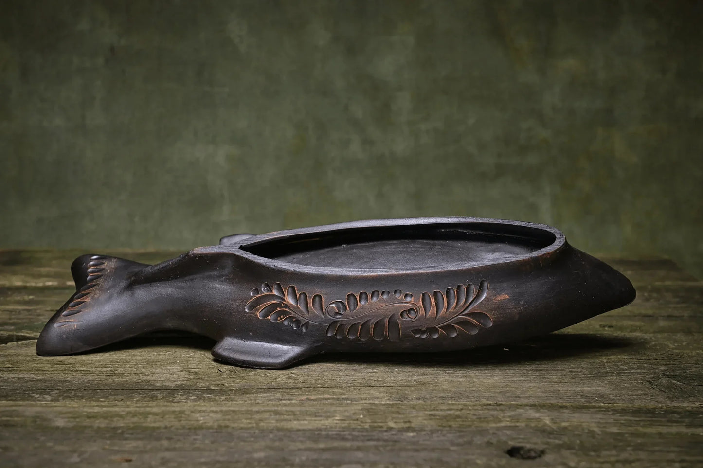 Handmade ceramic fish dish with carved pattern on rustic wood surface