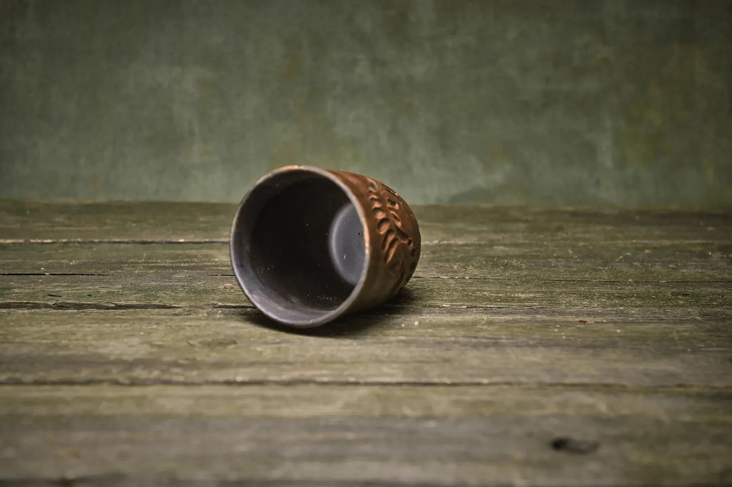 Handmade engraved clay pottery tumbler cup on rustic wooden surface, artisan homeware