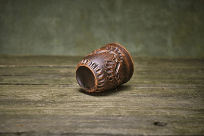 Handmade engraved ceramic clay tumbler cup on rustic wooden surface
