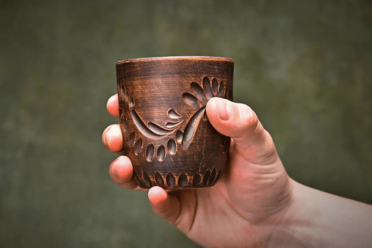 Hand holding a handmade engraved clay pottery tumbler, artisan-crafted cup