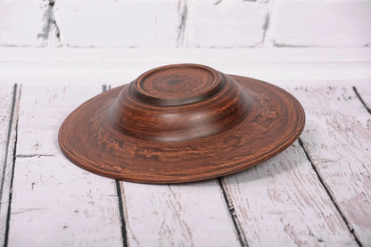 Handmade brown ceramic pasta bowl upside down on rustic white wooden surface