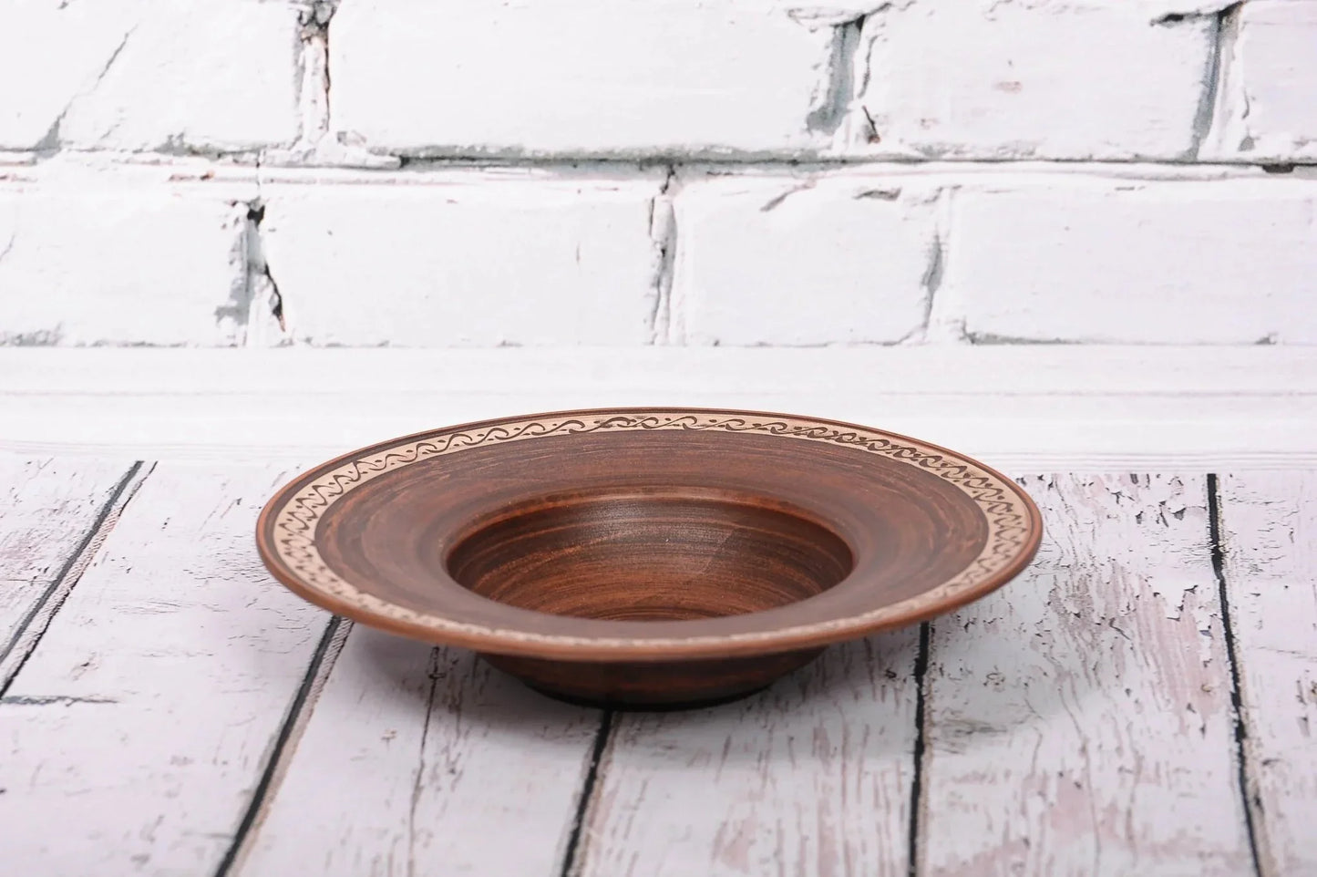 Handmade ceramic pasta bowl with decorative rim, artisan clay plate on rustic wood background