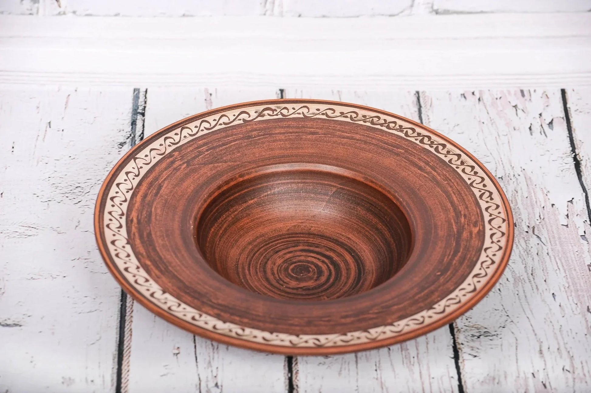 Handmade ceramic pasta bowl with decorative rim on rustic white wood background