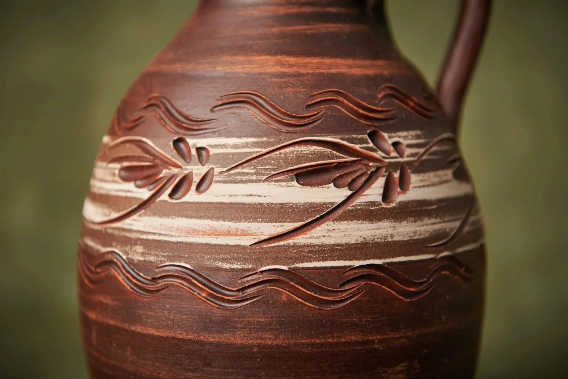 Handmade ceramic clay pitcher with carved floral pattern and earthy tones