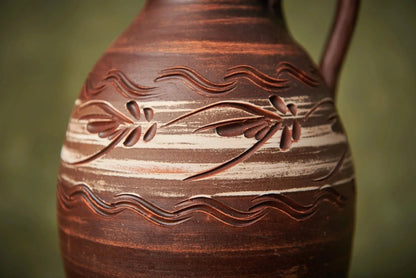 Handmade ceramic clay pitcher with carved floral pattern and earthy tones