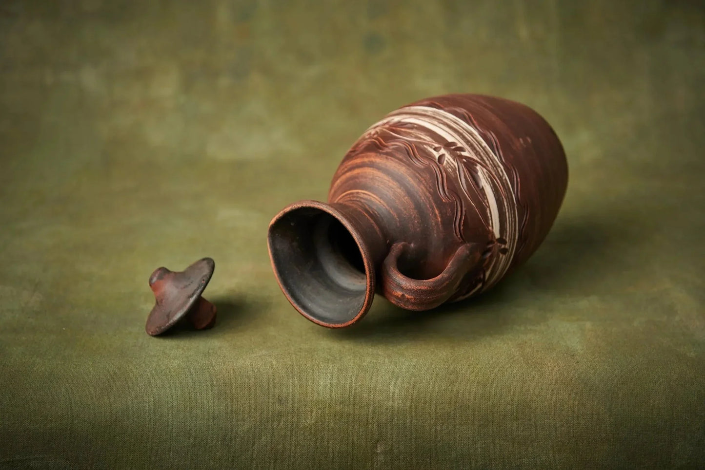 Handmade clay ceramic pitcher with lid, artisan homeware on green background