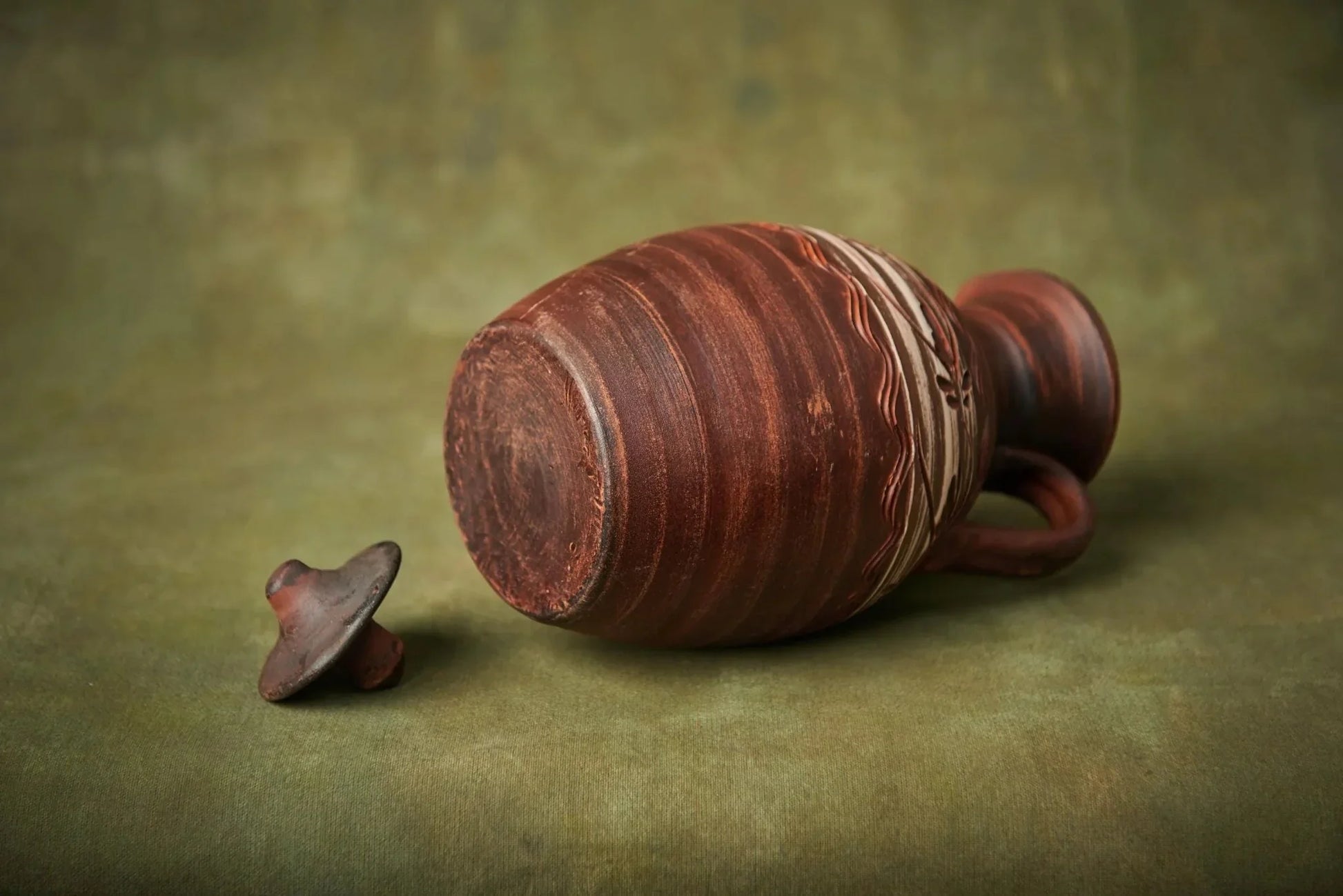 Handmade clay ceramic pitcher with lid, artisan pottery homeware on olive green background