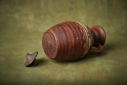 Handmade clay ceramic pitcher with lid, artisan pottery homeware on olive green background