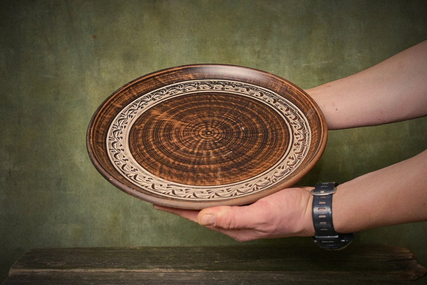 Hand holding a large handmade ceramic pizza plate with intricate clay design, artisan homeware