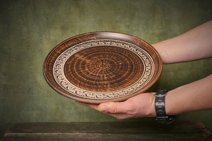 Hand holding a large handmade ceramic pizza plate with intricate clay design, artisan homeware
