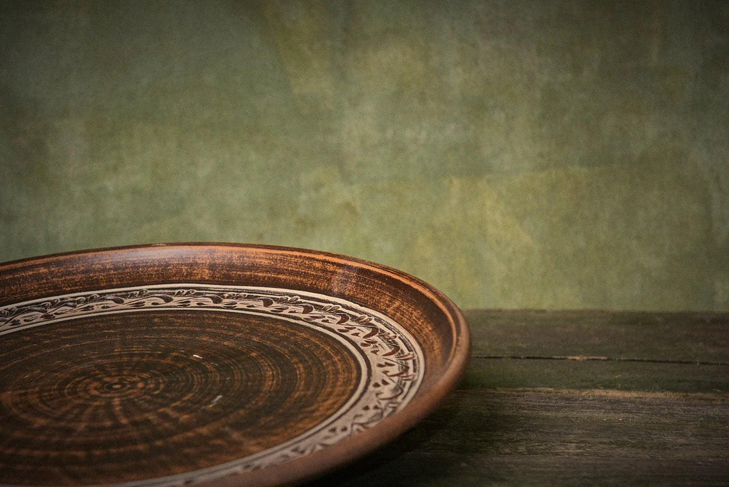Handmade ceramic clay pizza plate with intricate rim design on rustic wooden table