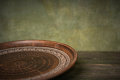 Handmade clay pizza plate with intricate rim design on rustic wood, artisan kitchenware