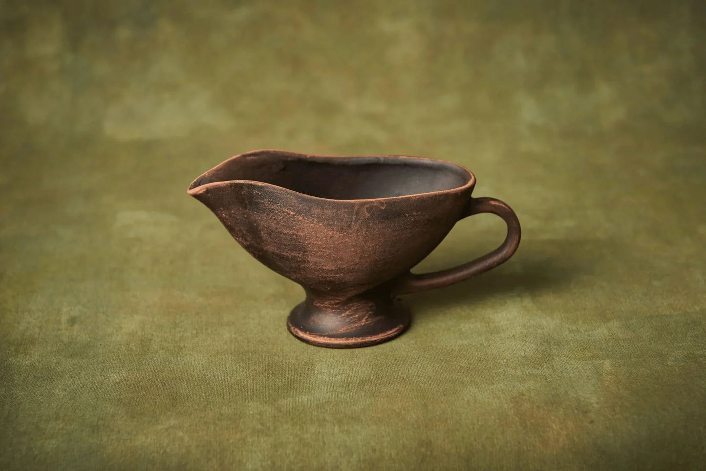Handmade ceramic sauceboat or creamer jug in rustic brown clay on a green background