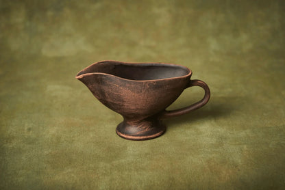 Handmade ceramic sauceboat or creamer jug in rustic brown clay on a green background