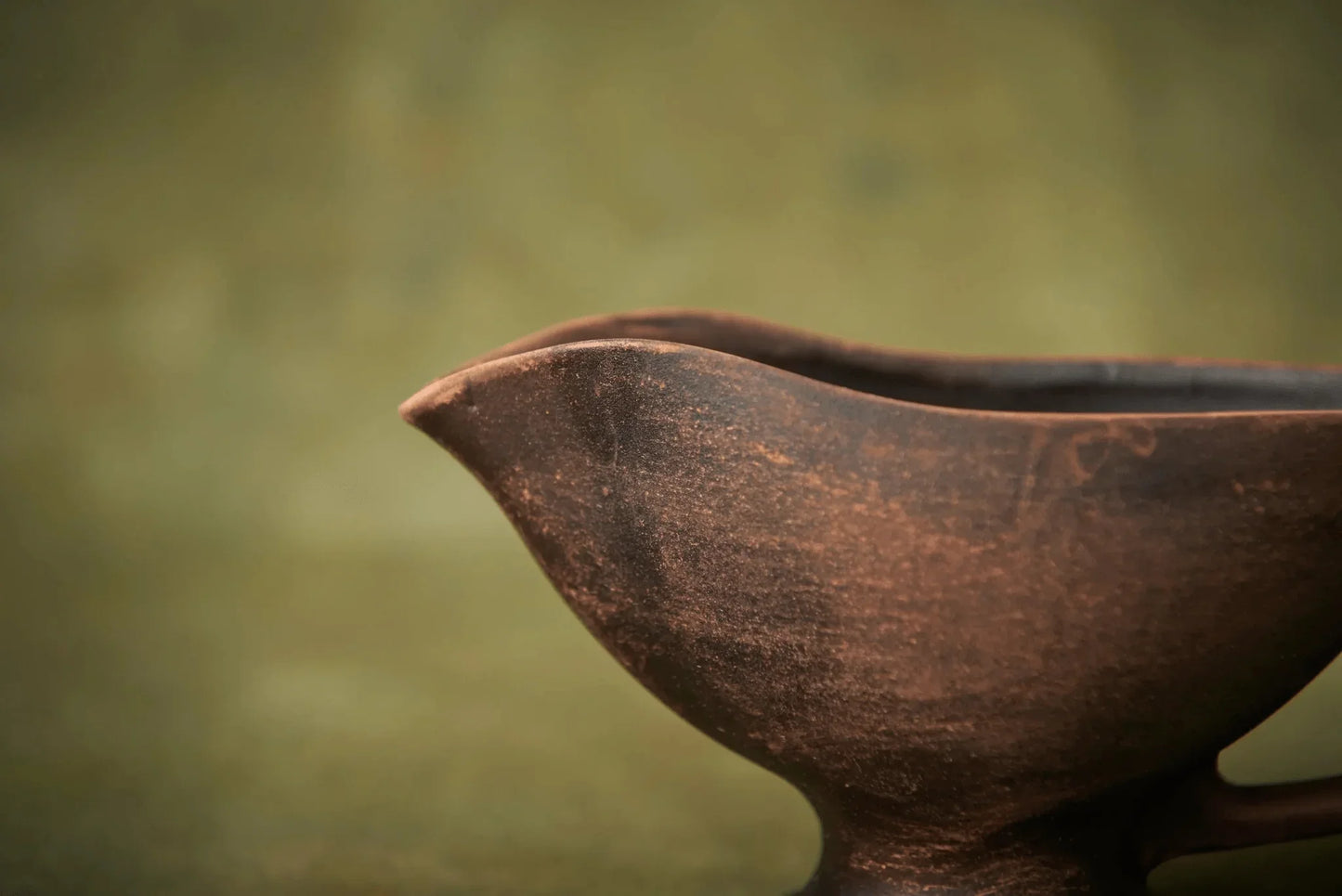 Handmade brown ceramic sauceboat jug on a green background, artisan clay homeware